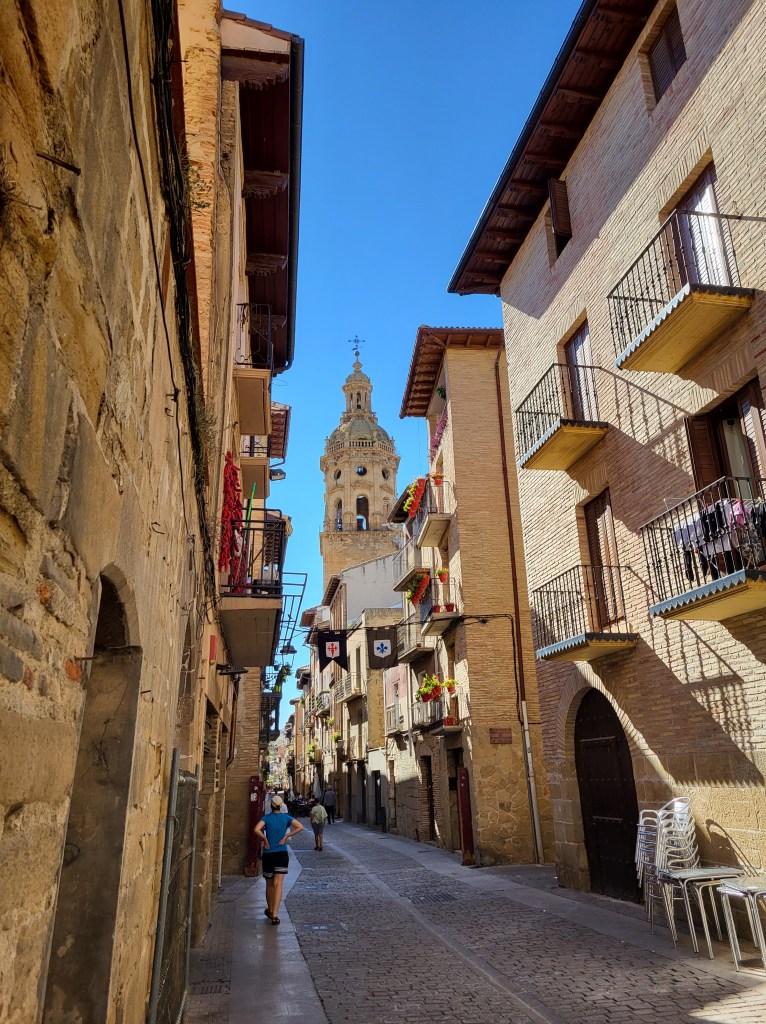 The spire of the cathedral rises above the main street into the blue skies in Puente La Reina, Navarra, Spain.