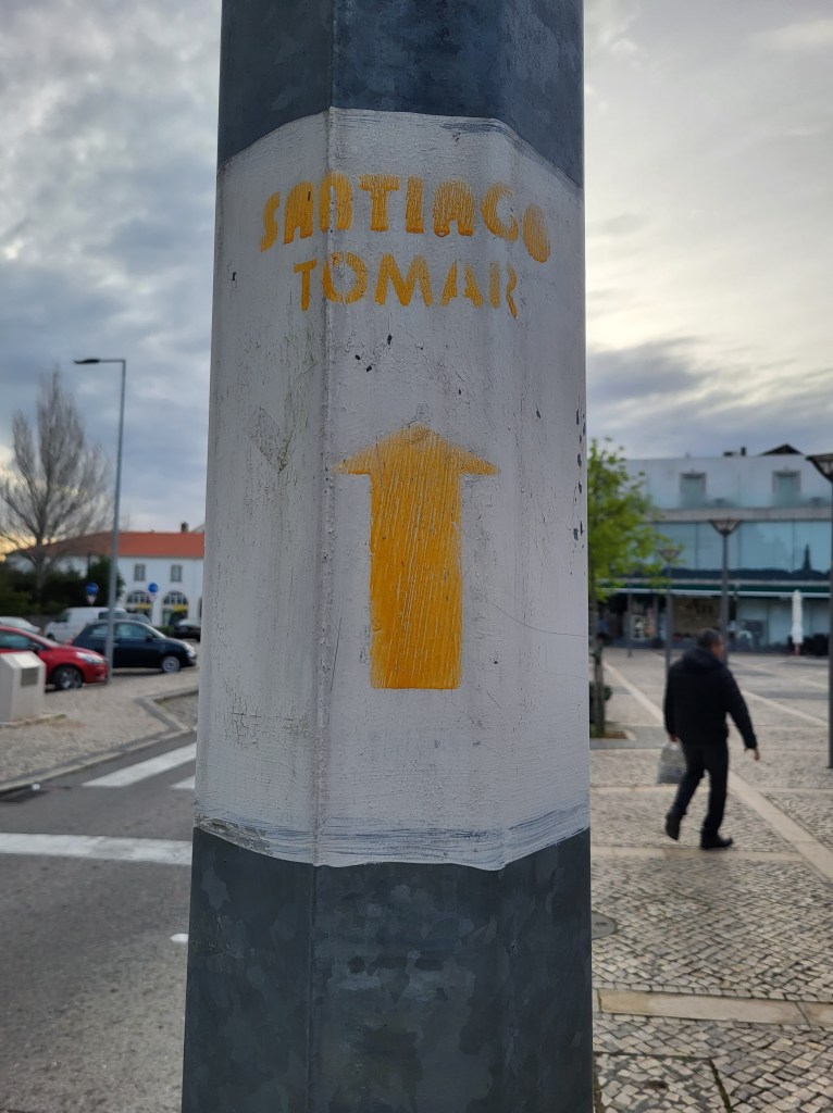 A yellow arrow painted on a utility pole pointing the way to Santiago de Compostela.